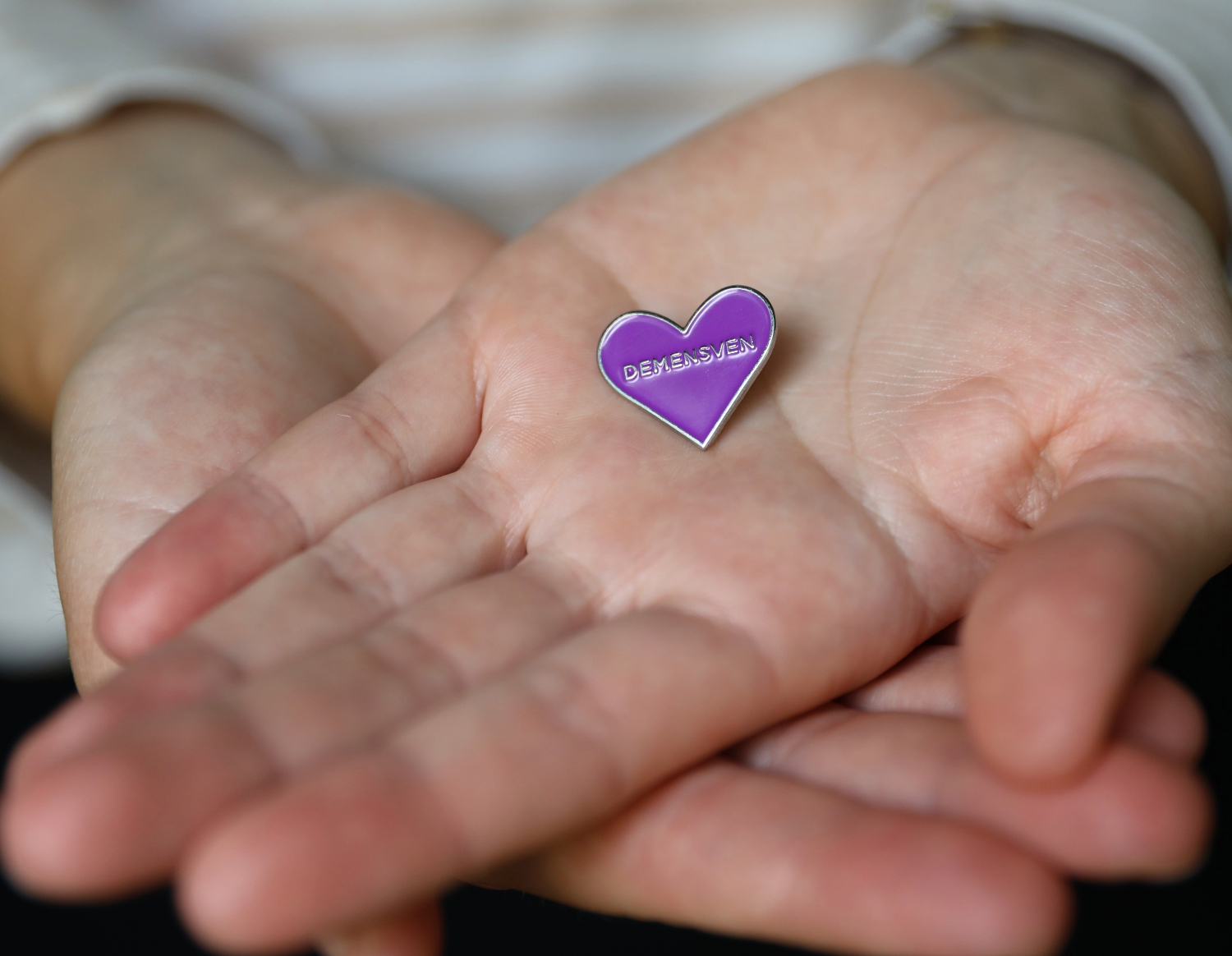 Nærbillede af to hænder, der holder en broche med demensven symbolet.
