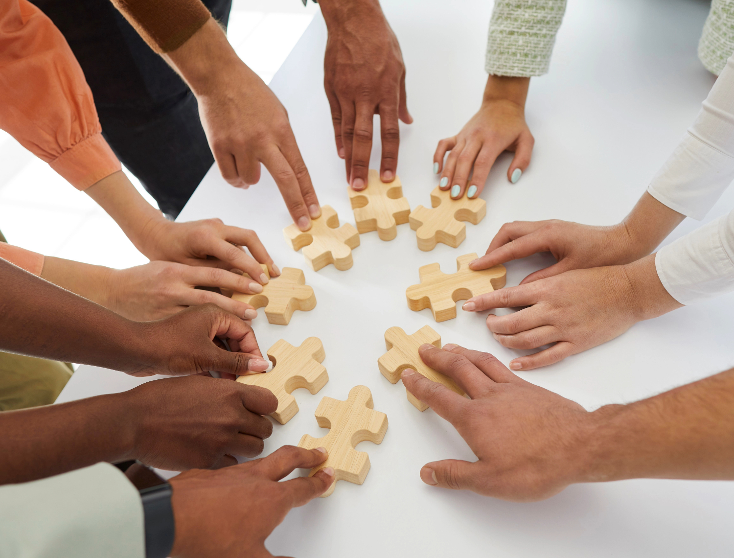 Nærbillede af mange hænder, der lægger brikker fra et puslespil.
