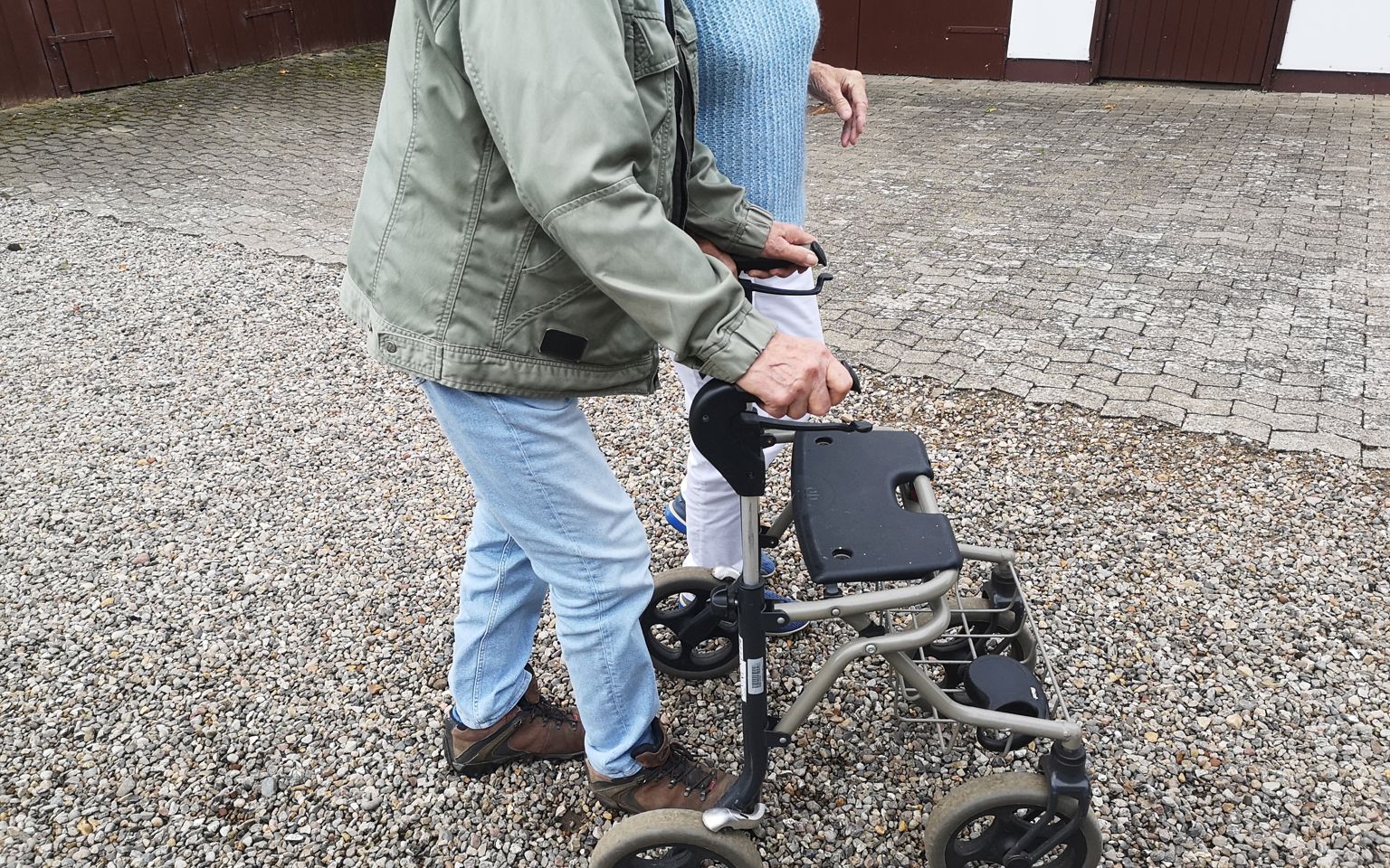 Et nærbillede af to personer, der går på en gårdsplads, hvoraf den ene går med rollator.
